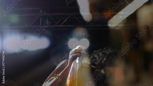 Spotlight revealing singer on stage gripping mic singing music to engage crowd under stage lights