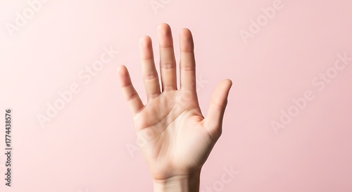 Close up of a single human hand with fingers spread wide open against a soft pastel pink background in studio lighting