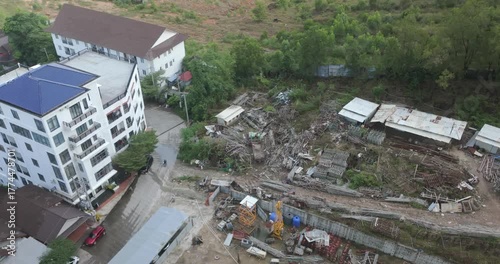 From a high angle, a crane loads long metal rods onto a truck in a chaotic scaffolding yard, while workers sort through massive scrap piles below.