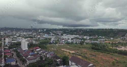 Zoomed out shot shows a heavy storm cloud looms over Sihanoukville's sprawling landscape, a mix of urban development, green hills, and cleared construction plots.
