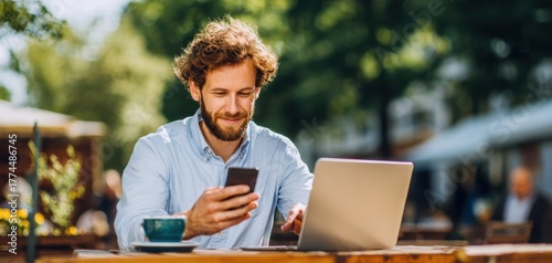The man working on a laptop while checking his smartphone at an outdoor cafe