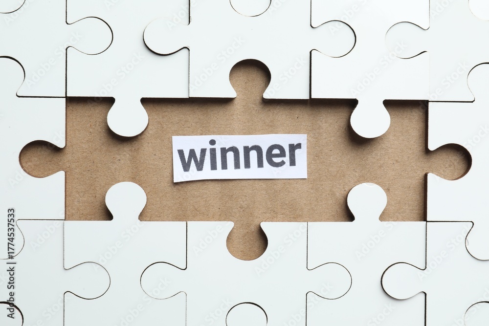 Fototapeta premium Paper note with word Winner and jigsaw puzzle pieces on carton, top view