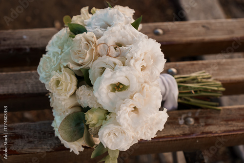 White Wedding Bouquet with Gold Rings on Wooden Bench in Soft Natural Light