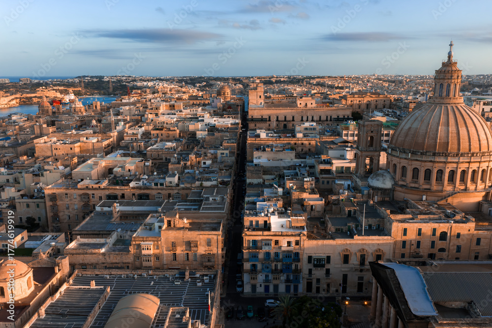Obraz premium Aerial sunset view of Valletta, Malta shows limestone blocks, Baroque forms, the basilica dome on the right, a straight street to Grand Harbour, and long evening shadows.