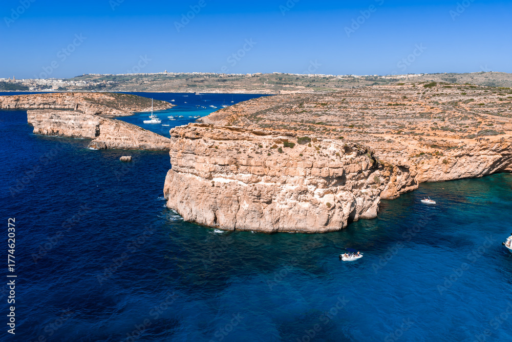 Obraz premium Aerial panoramic view of Blue Lagoon, Comino Island, Malta with boats and yachts. The scene looks north to Gozo, showing the narrow channel and bays at midday.