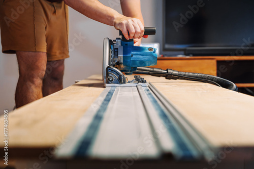 Carpenter Cutting Wooden Panel with Electric Circular Saw Using Track Indoors