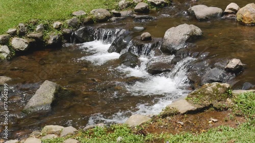 Looping footage of a clear mountain stream running over smooth rocks beside lush green grass. Ideal for meditation, eco backgrounds, or relaxation visuals