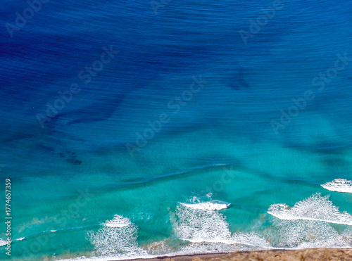 Blue ocean with waves and a sandy beach, top view.
