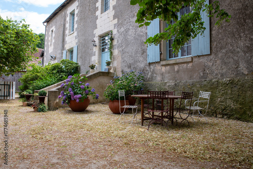Rustic Courtyard Of Stone House With Blue Shutters, Outdoor Table And Hydrangeas