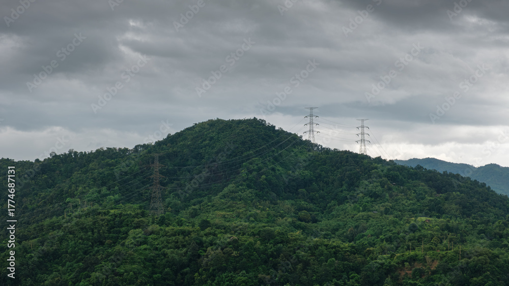 Obraz premium High-voltage power lines stretch across dense tropical greenery under a dramatic