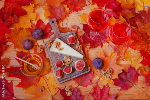 Two glasses of rose wine, parmesan cheese, figs, honey, walnuts  and colorful autumn maple leaves on wooden table. Top view.