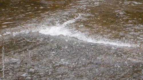 4K seamless loop of gentle river current creating wave-like ripples resembling ocean motion, captured in natural lighting with calm and relaxing atmosphere. Perfect for meditation or nature background