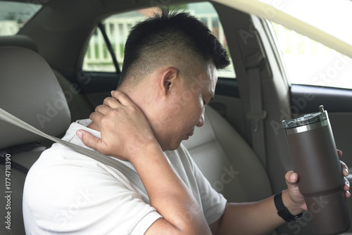 An asian male driver getting exhausted and feeling headache, wrist pain, neck ache, shoulder pain and backache, sitting inside his car, after driving car in traffic jam, causing stressed and anxiety.	