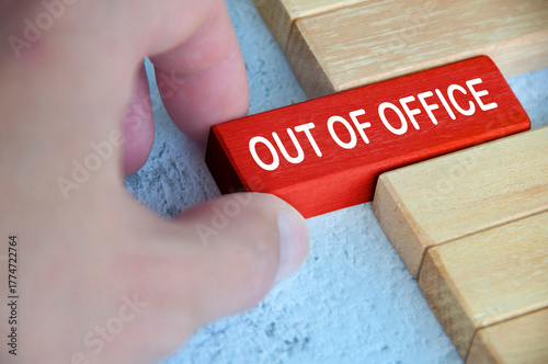 Hand pulling out a red wooden block with out of office text on. Getaway or on a vacation concept.