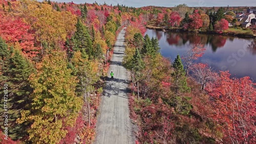 Cinematic drone shot Sunny Day Scene With Cyclist Traveling On Forest Trail Surrounded By Orange Trees And Water Views In Beechville Halifax Nova Scotia Canada.