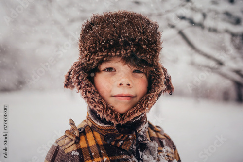 Portrait of a smiling boy wearing a hunters cap standing in a snowy forest landscape in winter, USA