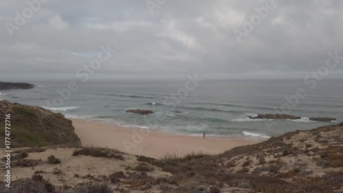Aerial traveling shot of a lone fisherman walking along a cloudy beach in Alentejo, Portugal - 1832