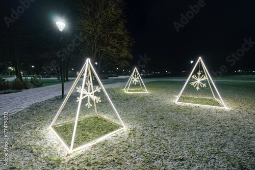 Minimalist Illuminated Christmas Pyramids with Snowflakes in Park on Dark Winter Night