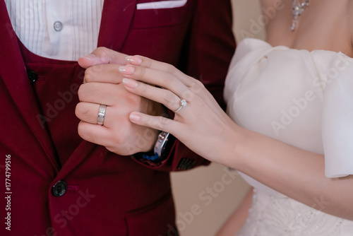 The bride's left hand holding the wedding ring is holding the groom's left hand who is also wearing a wedding ring.