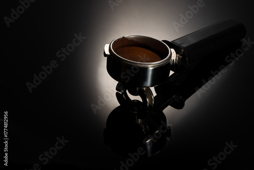 Espresso machine portafilter handle over gradient black background with reflection.