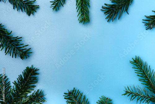 Top view of green fir tree branches arranged around the edges on a blue background with copy space. Minimal winter and Christmas composition for greeting cards