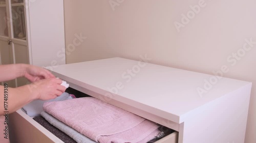 woman carefully places neatly folded children's clothes into the top drawer of a white dresser after laundry completion in a nursery organization routine