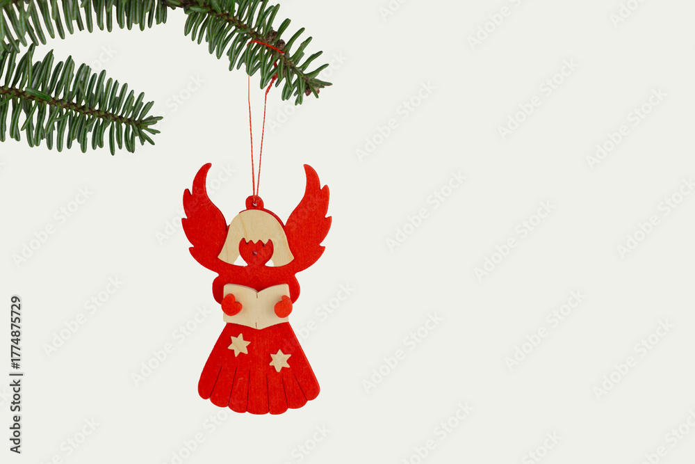 Obraz premium red wooden Christmas angel ornament with stars hanging from a pine branch on a white background