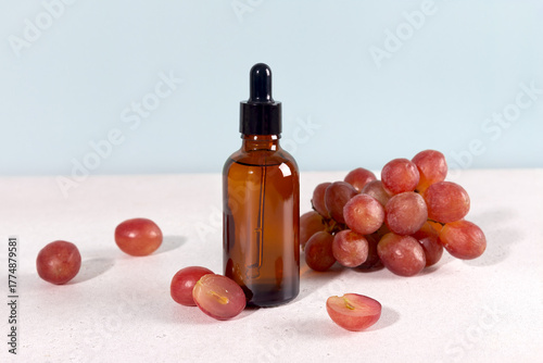Grape seed oil in dropper bottle with fresh green grapes on a blue background. Skin care concept.