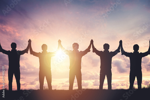 Silhouette of people holding hands against sunset background, concept of peace and victory