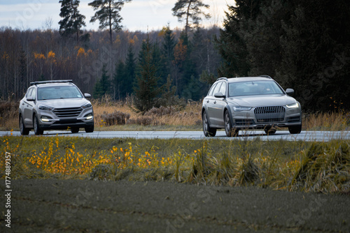 Two cars driving on countryside road through autumn forest, transportation and travel concept, rural mobility and traffic safety background with natural landscape