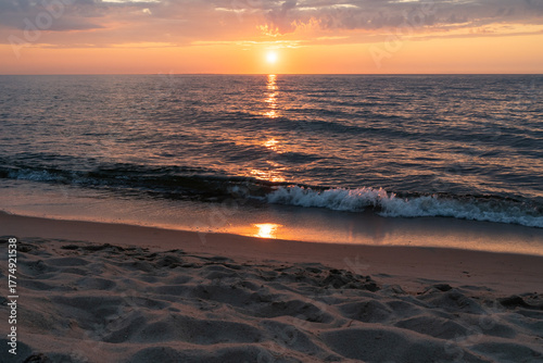 Fototapeta Naklejka Na Ścianę i Meble -  Golden sunset reflects on the Baltic Sea waves lapping a tranquil sandy beach on the coast of Estonia.