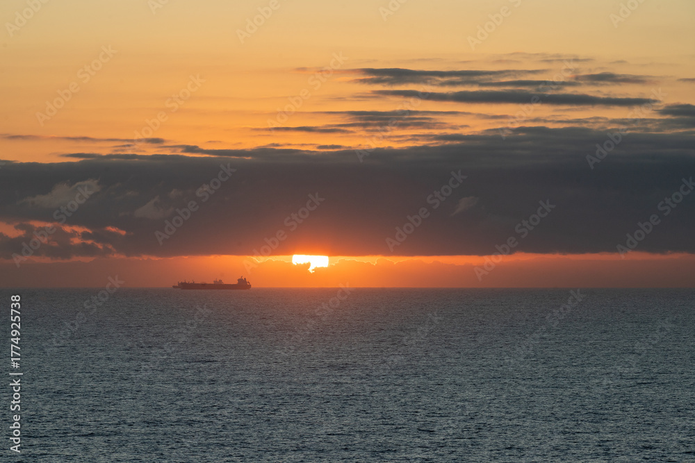 Fototapeta premium Beautiful sunset over ocean with cargo ship sailing near horizon in calm waters