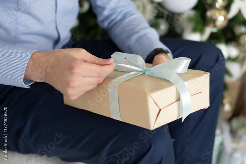 Male hand holding Christmas gift on new year tree background