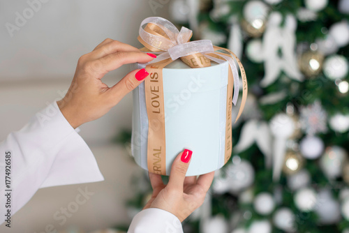 
Female hands holding gift box decorated with golden ribbon, on Christmas tree background