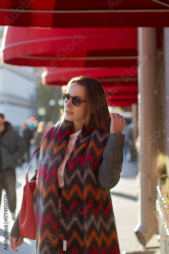 Young beautiful woman in grey coat and red scarf walking along the street