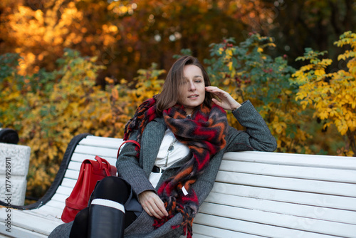 Beautiful business woman in a cozy scarf on an autumn park bench