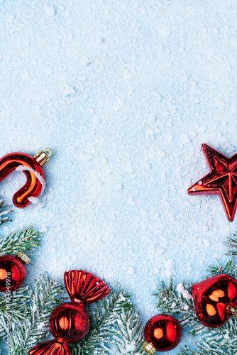 Festive Christmas composition with red ornaments, candy cane, and frosted fir branches on light blue snowy background.