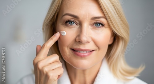 Mature woman applying skincare cream to face, smiling with fresh and glowing skin