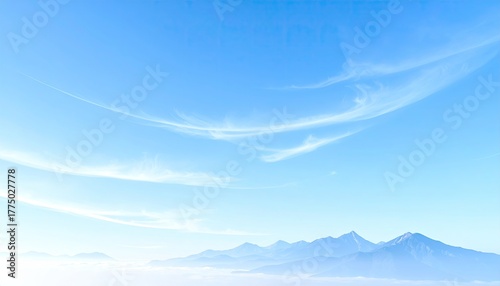 Vast expanse of pale blue sky filled with wispy white clouds above distant misty mountains under soft natural light