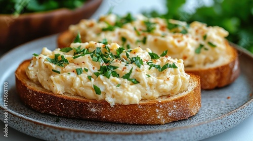 Close-up of two slices of toasted bread topped with creamy egg salad garnished with chopped green herbs on a ceramic plate