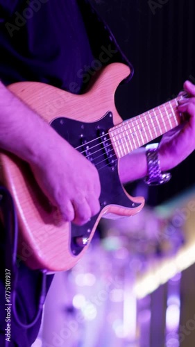 Electric musician under purple lighting, Performer playing guitar on vivid stage, Electrified performer focusing on rhythm and lead guitar under vibrant purple