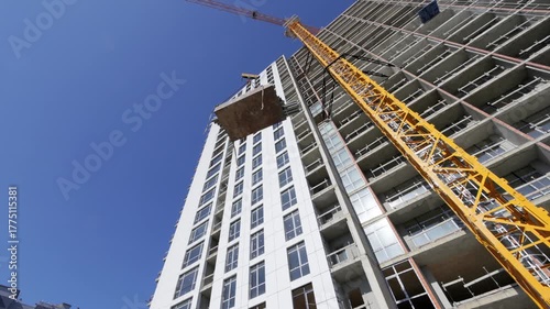 Urban building construction underway, Tower crane elevating significant concrete for skyscraper, City skyline background with workers managing heavy construction