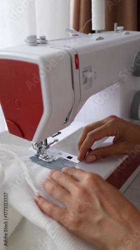 White garment under presser, caucasian costume maker guiding fabric steadily across needle, soft daylight and careful hand placement during assembly and hemming