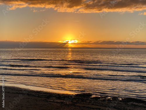 Intense Golden Sunset Over the Ocean Horizon with Sunburst Through Clouds and Dramatic Rays