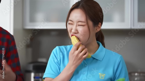 A young woman in a blue polo shirt accepts a banana from another person and takes a thoughtful bite