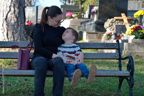Mother and her little boy sitting on the bench in a cemetery