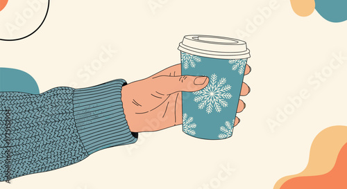A hand in a cozy blue knitted sweater holds a disposable coffee cup with white snowflakes, set against a warm cream background, evoking winter comfort.