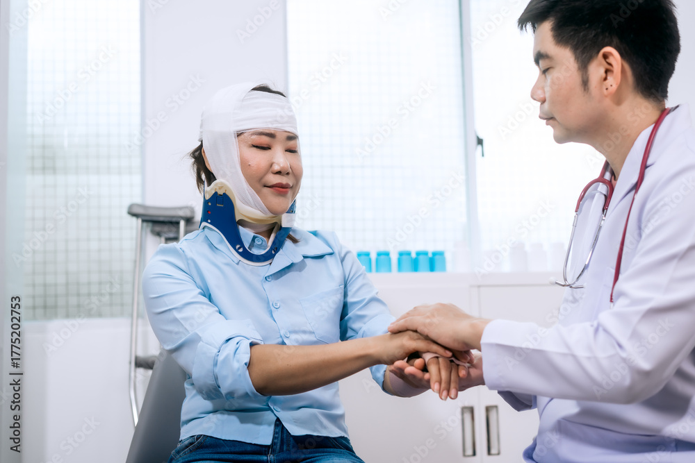 Obraz premium A male doctor gently examines and reassures an Asian female patient wearing a head bandage and neck brace after an accident,reflecting empathy, recovery care,professional medical support in a clinic