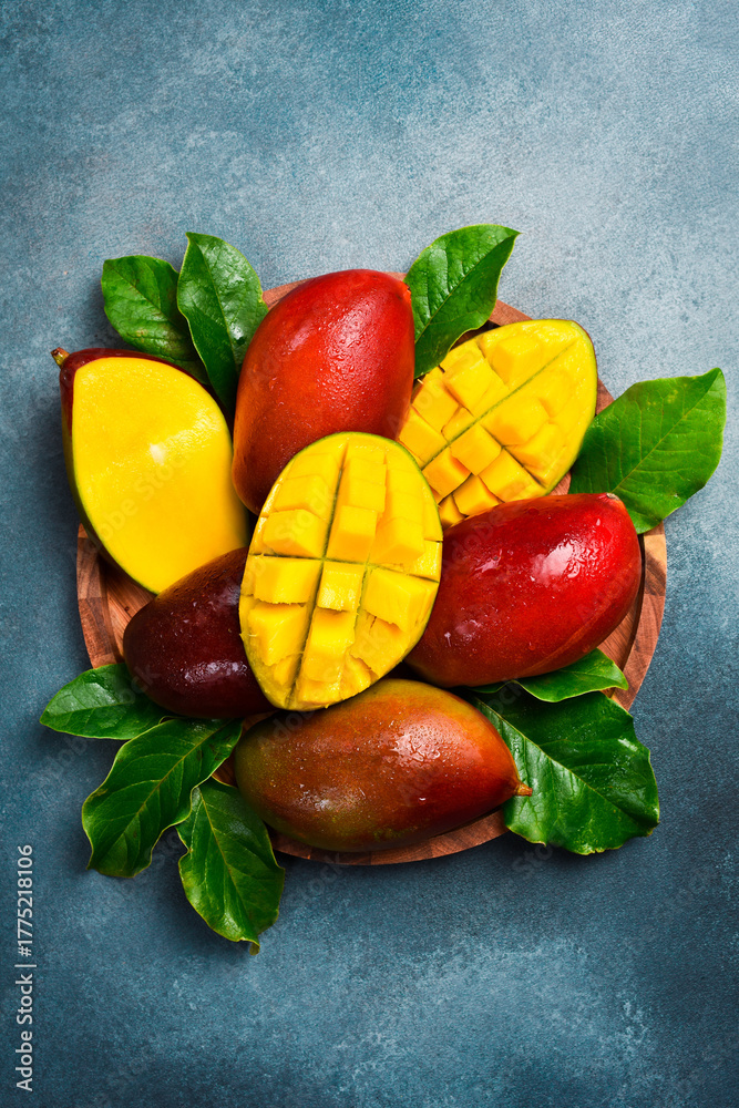 Fototapeta premium Set of ripe mango fruits and leaves on a wooden plate. On a concrete stone background. Tropical fruits.