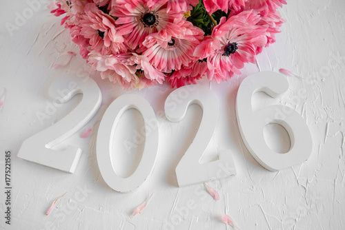 Year 2026 numbers positioned on a white textured background with a vibrant bouquet of pink anemone flowers and scattered petals above, symbolizing new beginnings and future celebrations